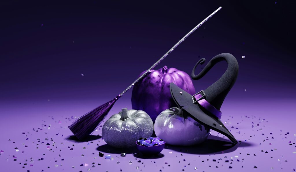 A Halloween-themed still life featuring metallic purple and silver pumpkins, a glittering broom, a witch’s hat with a purple band, and scattered confetti on a purple surface.